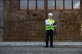 Male architect in white hard hat and reflective vest standing, working on digital tablet at building site. High skilled Royalty Free Stock Photo