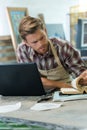 male artisan working at desk with laptop and book