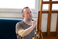 Male artist painter working in workshop with canvas on wood drawing board easel in art paint studio. Portrait of artist.