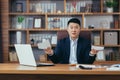 Male Asian businessman refused a loan, frustrated looking at the camera, working in a classic office