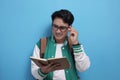 Male Asian student studying hard, reading a book against blue background Royalty Free Stock Photo