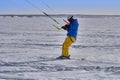 A male athlete engaged in snow kiting on the ice of a large snowy lake. He goes skiing in the snow