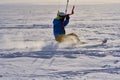 A male athlete engaged in snow kiting on the ice of a large snowy lake. He goes skiing in the snow.