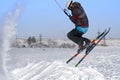 A male athlete engaged in snow kiting on the ice of a large snowy lake. He performs the jump. Winter sunny frosty day.