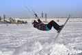 A male athlete engaged in snow kiting on the ice of a large snowy lake. He performs the jump. Winter sunny frosty day. Close-up