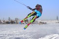 A male athlete engaged in snow kiting on the ice of a large snowy lake. He performs the jump. Winter sunny frosty day.