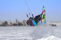 A male athlete engaged in snow kiting on the ice of a large snowy lake. He performs the jump. Winter sunny frosty day.