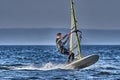 A male athlete is interested in windsurfing. He moves on a Sailboard on a large lake