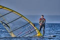 A male athlete is interested in windsurfing. He moves on a Sailboard on a large lake