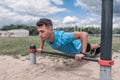 Male athlete is pushing up from horizontal bar, training is powerful, in summer in city, in afternoon in fresh air