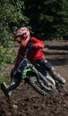 Male athlete riding a dirt bike through a muddy forest path almost falling off from it