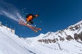 A male athlete skier in an orange trigger makes a jump jump with a grab with flying snow powder against the background