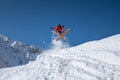 Male athlete skier in an orange trigger makes a jump trick with flying snow powder against the backdrop of snow-capped