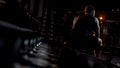 Male athlete tired after workout sits on bench, hunches up alone in evening gym
