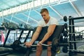 Male athletic exercising with barbell on preacher bench in fitness center