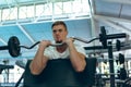 Male athletic exercising with barbell on preacher curl in fitness center