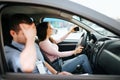 Male auto instructor takes exam in young woman. Shamed guy cover face with hand. Female student driving car and taking