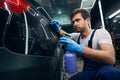 Car repairman sprinkling car surface with liquid