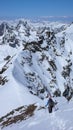 Male back country skier hiking along a narrow snow ridge with a great mountain landscape behind him