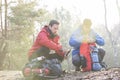 Male backpacker with friend whittling wood in forest