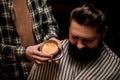 male barber holds round jar of hair styling gel near the head of male client.