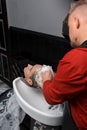 Male barber washes the hair and head of a young guy's client with foam over the sink before a haircut in a barbershop