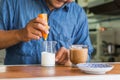 Male barista making froth milk in a beaker with frother for making a latte coffee at the wooden counter bar