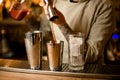 Male barman pours red drink from metal jigger into shaker on bar counter