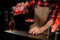 Male bartender accurate pours red campari drink from mixing cup to wineglass Royalty Free Stock Photo