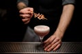 Male bartender decorated pink cocktail with a white foam with a bacon on the skewer