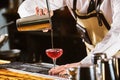 Male bartender is making cocktail pouring alchohol from shaker