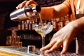 Male bartender is making cocktail pouring alchohol from shaker