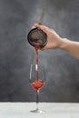 Male bartender is making cocktail pouring alchohol from shaker to wine glass at grey wall background