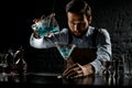 Male bartender pouring a blue color alcoholic cocktail from the measuring cup with strainer to a martini glass Royalty Free Stock Photo
