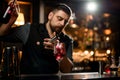 Male bartender pouring a red liqour from the jigger to a cocktail glass holding a bottle Royalty Free Stock Photo