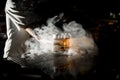 Male bartender serving a light brown alcoholic drink with the ice cube in the glass in the steam