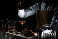 Male bartender spraying on a brown alcoholic drink in a martini glass with orage zest juice