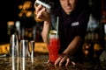 Male bartender sprinkling to the cocktail glass decorated with ice, lime and tropical leaf a sugar powder