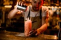 Male bartender sprinkling to the red cocktail in the glass with a crushed ice with spices