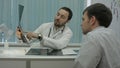 Male bearded doctor in clinic show x-rays to male client.