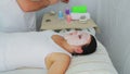 A male beautician puts fresh cucumbers in the spa salon on the client's face