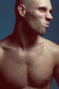 Male beauty concept. Handsome male model with earring posing over blue background. Perfect skin, shaved head, hairy muscular body Royalty Free Stock Photo