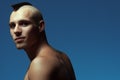 Male beauty concept. Portrait of handsome muscular male model posing over blue background. Shaved head with upright crest. Healthy