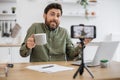 Male blogger holding cup and talking with followers at home