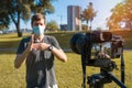 A male blogger in a protective mask shoots a video with a digital camera outdoors on a sunny day. Remote freelance work during a