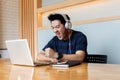 Male blogger watching video in social networks via headphones while updating software on laptop computer, Asian man listening audi