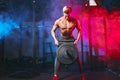 Male bodybuilder champion exercises with heavy weight barbell plate in gym.