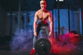 Male bodybuilder champion exercises with heavy weight barbell plate in gym.