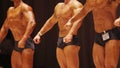 Male bodybuilders boasting of muscular bodies on stage, result of hard workouts