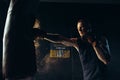 Male boxer in boxing gloves hitting punching bag at training in dark gym